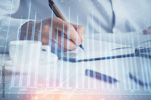 Double exposure of man's hands writing notes of stock market with forex chart.