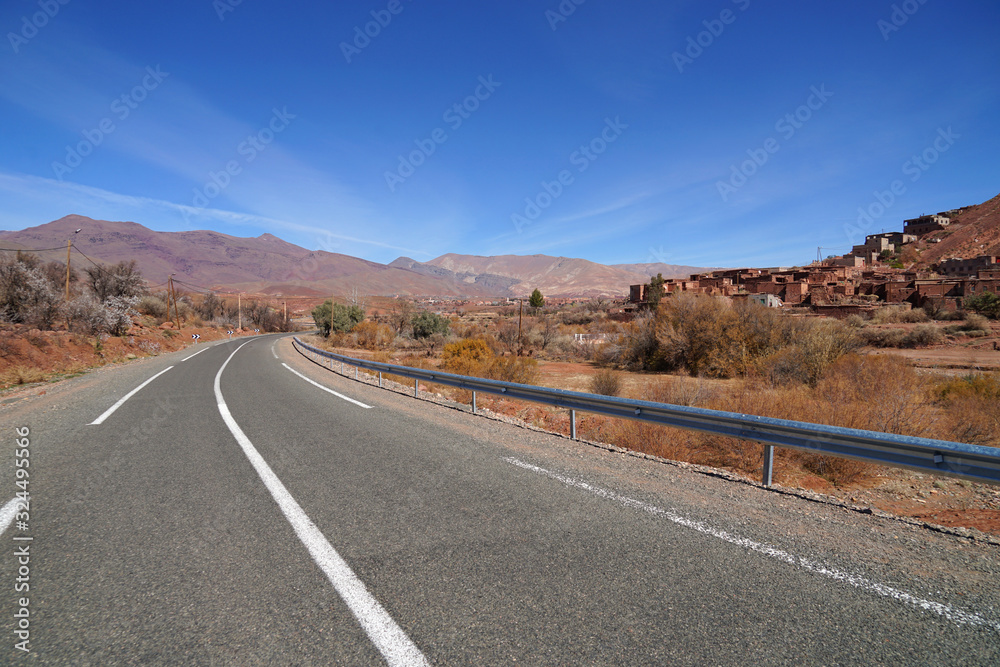 Well maintained road across Atlas Mountains with Berber village on background, Morocco