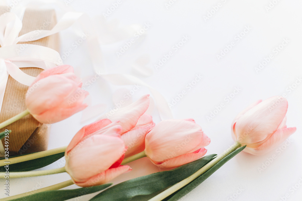 Fototapeta premium Happy womens day. Pink tulips and gift box with ribbon on white background. Stylish tender image. Greeting card with space for text. Happy Mothers day. Wedding or valentine celebration