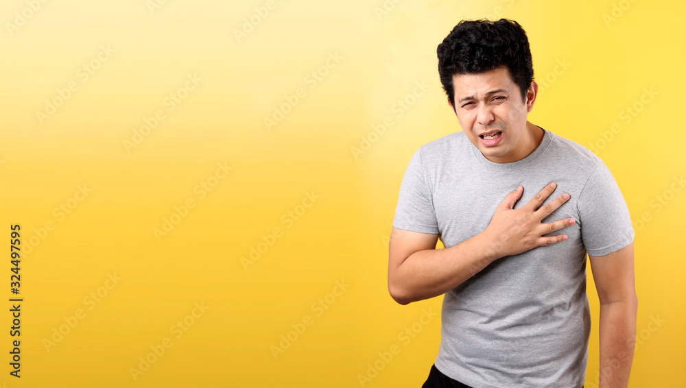 Handsome Asian man with heart pain,on yellow background in studio With copy space. Handsome Asian man with heart pain,on yellow background in studio With copy space.