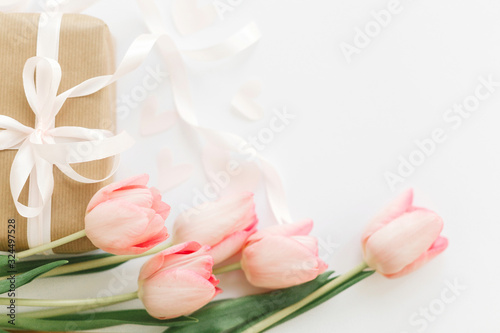 Fototapeta Naklejka Na Ścianę i Meble -  Happy Mothers day. Pink tulips with ribbon and gift box on white background, flat lay. Stylish tender image. Happy womens day. Greeting card with space for text. Wedding or valentine mockup