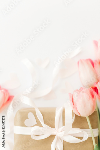 Pink tulips with ribbon and gift box on white background, flat lay. Stylish vertical image. Happy womens day. Greeting card with space for text. Happy Mothers day. Wedding or valentine mockup