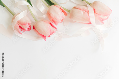 Happy Mothers day. Pink tulips with ribbon and hearts on white background, flat lay. Stylish soft spring image. Happy womens day. Greeting card mockup with space for text. Hello spring