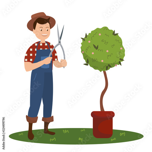 Smiling man in a checkered red-white shirt and blue overalls holding a pruning shears in his hands standing next to a green flower in pot. Isolated on white background. Vector stock illustration