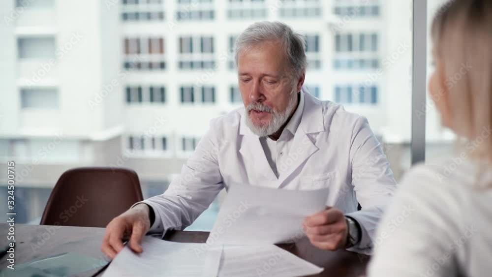 Team of adult and young doctors discussing over medical report in modern meeting office room of the hospital against a large window. Concept of team of doctors working together at the clinic.