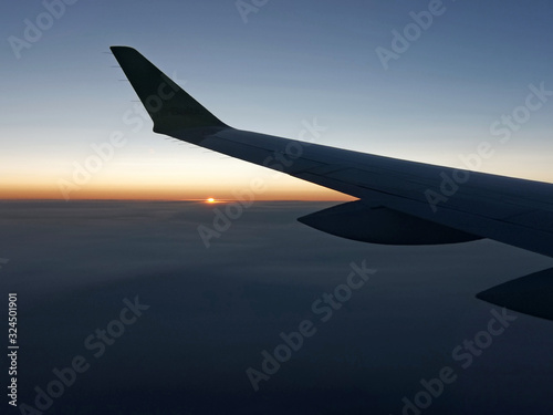 Sunset from a plain. View through the window of an aircraft. Wing of the plane above clouds