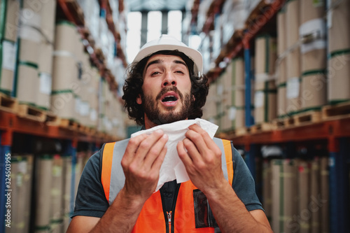 Young caucasian warehouse supervisor sneezing while feeling sick of cold