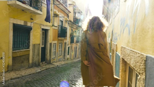 girl walks along old city street on windy day backside view