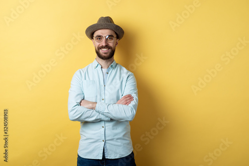 Man wearing in casual clothing, glasses and hat standing folded hands and cheeerful smiling against an yellow background. Confidence emotion © speed300