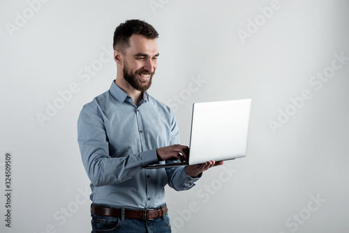 Bild auf Leinwand Cheerful guy in blue shirt stands holding an open  laptop against a white studio