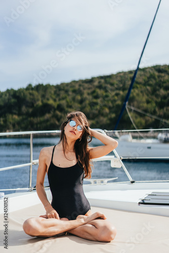 Young healthy and calm woman doing yoga on sailing yacht boat in sea at island background © teksomolika