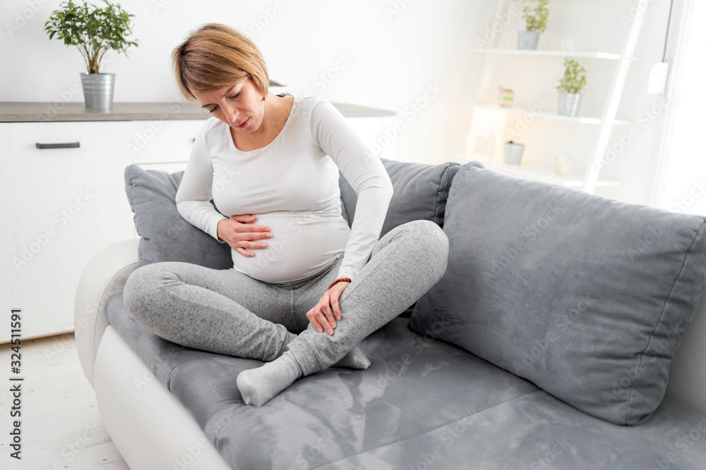 Pregnant tired exhausted woman with stomach, leg and pain issues at home on a couch, being sick. Pregnant tired exhausted woman with stomach, leg and pain issues at home on a couch, being sick.