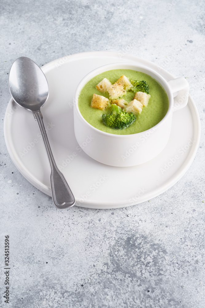 Vegetarian Broccoli green cream soup puree with croutons in a white cup on gray stone table. Minimalism concept for design. Copy space. Vegetarian Broccoli green cream soup puree with croutons in a white cup on gray stone table. Minimalism concept for design. Copy space.