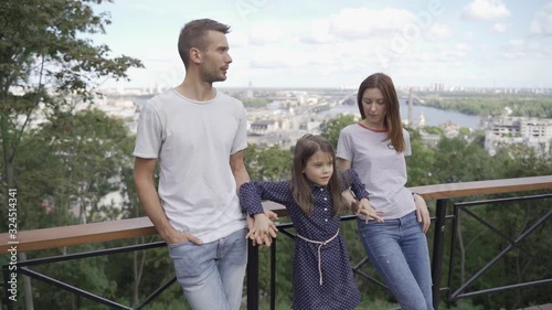 Beautiful young family on a walk, parents with daughter in a park on an alley