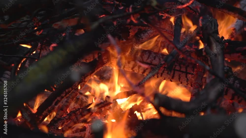 Firewood burns in a flame of fire in the evening. Tourist camp by the fire. Close-up of flame, branches and firewood burning and smoldering at dusk. Firewood burns in a flame of fire in the evening. Tourist camp by the fire. Close-up of flame, branches and firewood burning and smoldering at dusk.