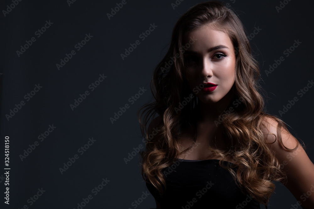 Close up beauty portrait of young beautiful girl in shadow with long curly hair wearing a black top. Text space.