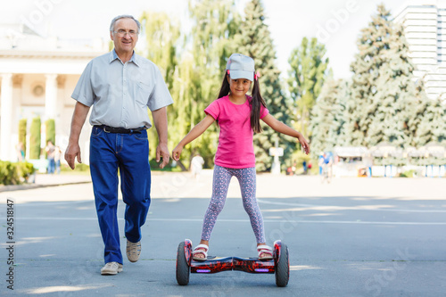 Little smiling girl learning to ride a hoverboard with her parents outdoors