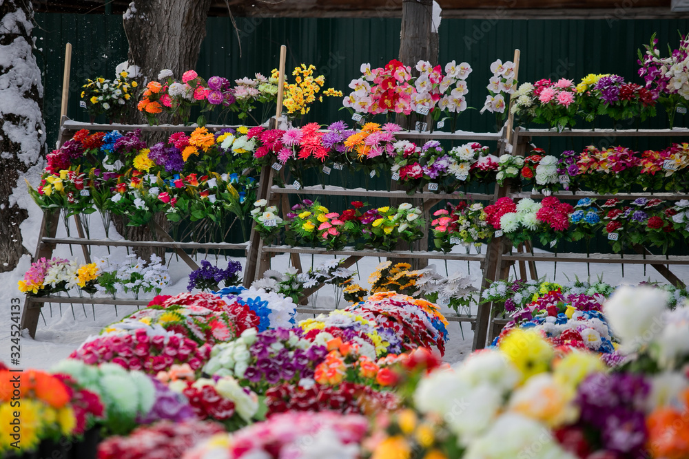 Fototapeta premium a point of sale with many artificial flowers, bouquets and wreaths near the cemetery sells jewelry and traditional offerings to the graves of the dead in memory of living relatives