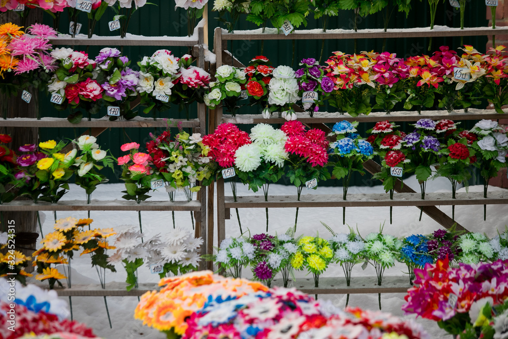 a point of sale with many artificial flowers, bouquets and wreaths near the cemetery sells jewelry and traditional offerings to the graves of the dead in memory of living relatives a point of sale with many artificial flowers, bouquets and wreaths near the cemetery sells jewelry and traditional offerings to the graves of the dead in memory of living relatives