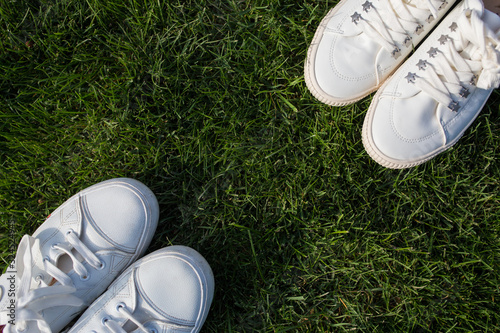 Women's and men's white sneakers on green grass. The guy and the girl are facing each other. View from above.