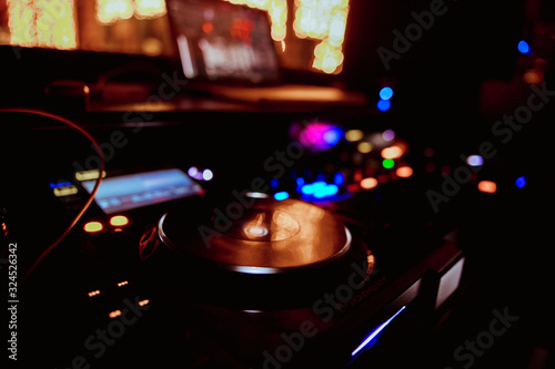 Club DJ playing mixing music on vinyl turntable at party wearing sunglasses with lens flare from nightlife lights.