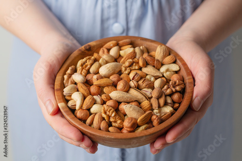 Woman hands holding bowl with mixed nuts, selective focus. Healthy vegetarian food and snack. 