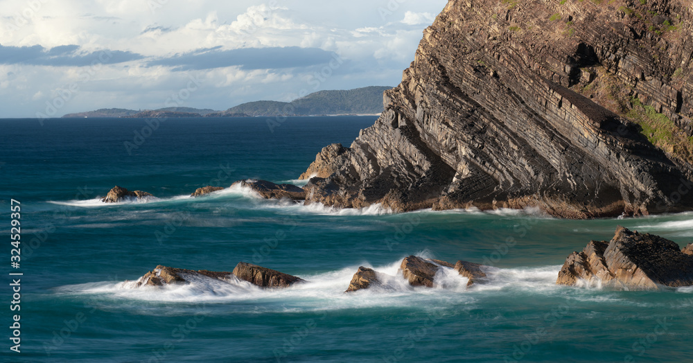 Naklejka premium Soft waves gently crash onto the rocks of crescent head with beautiiful morning light in australia