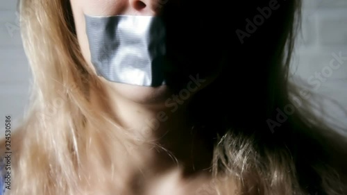 Upset girl with self-adhesive tape over her mouth. Portrait of a close-up of a girl with a taped mouth. Concept of slavery, violence.