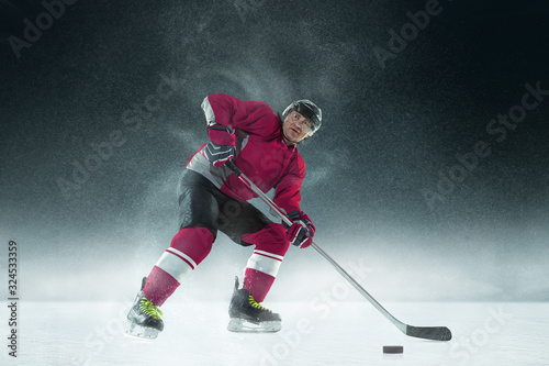 Moment. Male hockey player with the stick on ice court and dark background. Sportsman wearing equipment and helmet practicing. Concept of sport, healthy lifestyle, motion, movement, action.