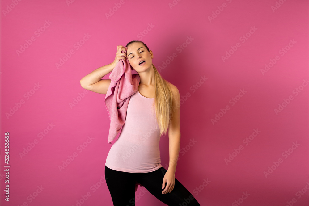 Young fit woman tired after workout with towel on her shoulders on pink background Young fit woman tired after workout with towel on her shoulders on pink background