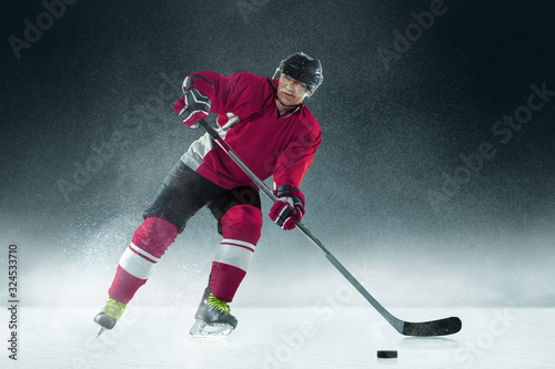 Fighting. Male hockey player with the stick on ice court and dark background. Sportsman wearing equipment and helmet practicing. Concept of sport, healthy lifestyle, motion, movement, action.