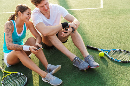 Attractive healthy tennis players couple using mobile phones