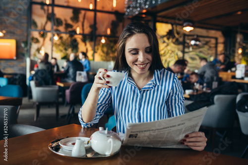young woman enjoying tea and reading press in cafe bar