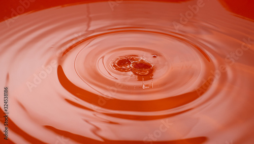 Water drop falling and drips in colored glass. Water drop splash and make perfect circles and crowns on water surface