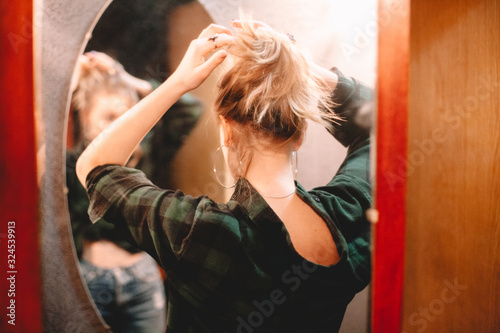 Tableau sur toile Young woman tying hair while looking at herself in the mirror at home getting re