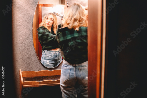 Young woman using curling iron looking at herself in the mirror at home preparing to go out