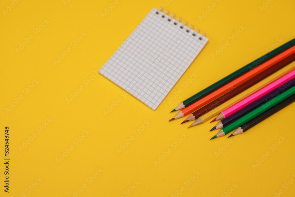 Colored pencils and a white sheet of notepad on a yellow background, space for text. Flat lay.