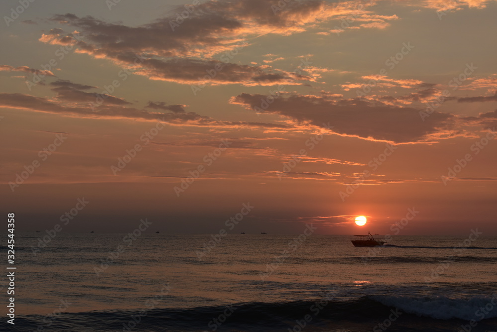 a boat just below the sun during a sunset in a ocean in goa