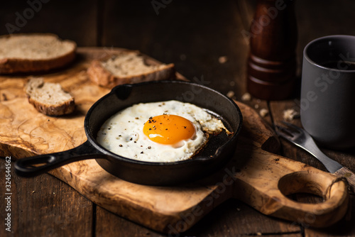 Fried egg, bread slice and black coffee.Chopping board. Dark, wooden, rustick table.