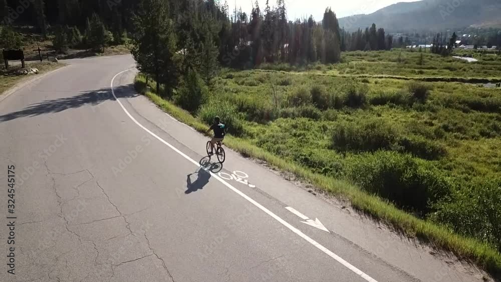 solo cyclist travels down a road next to swamp wetlands, aerial tracking shot from side solo cyclist travels down a road next to swamp wetlands, aerial tracking shot from side