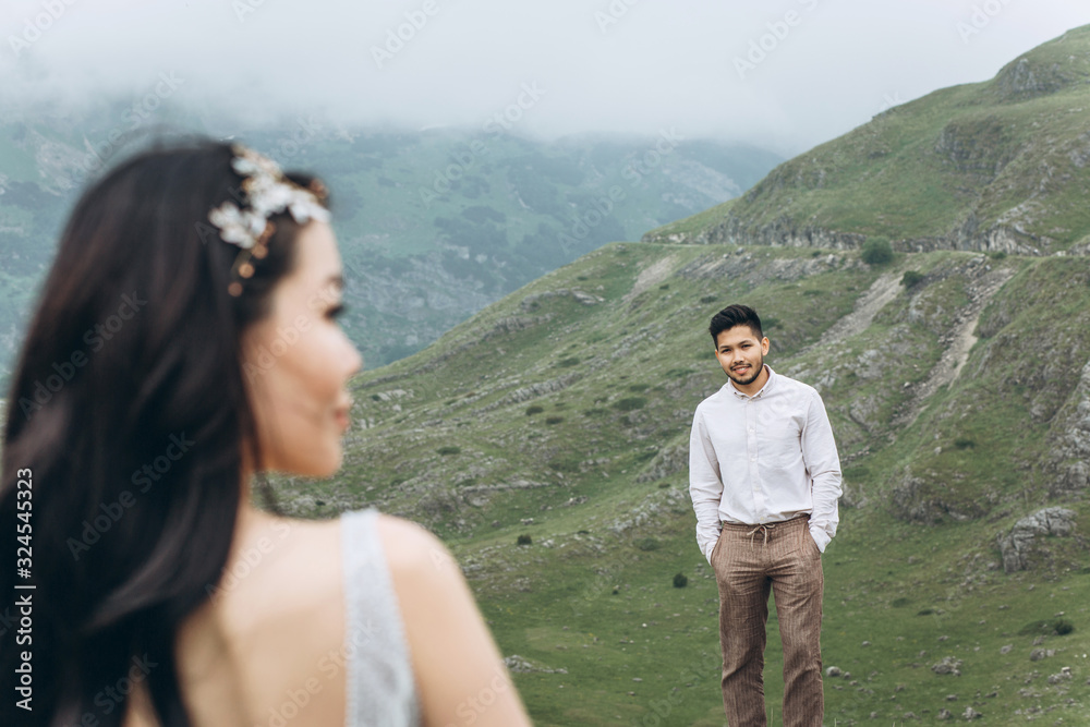 Kazakh groom stands on a background of mountainous terrain and looks at his bride.