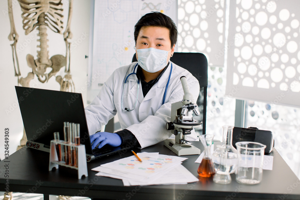 Portrait of Asian scientist doctor man sitting at the table and making notes on laptop, working with microscope and test tubes in laboratory. Medical, healthcare and pharmaceutical research concept. Portrait of Asian scientist doctor man sitting at the table and making notes on laptop, working with microscope and test tubes in laboratory. Medical, healthcare and pharmaceutical research concept.