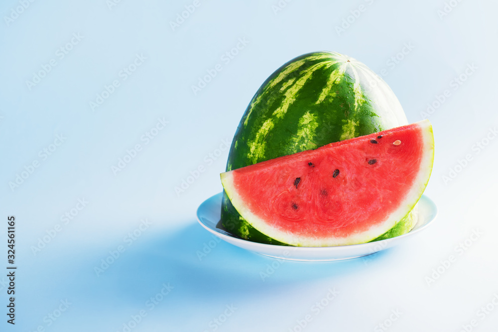 Half a watermelon and a slice of watermelon aer on a plate on a pastel blue background. Healthy Summer Snack Concept Half a watermelon and a slice of watermelon aer on a plate on a pastel blue background. Healthy Summer Snack Concept