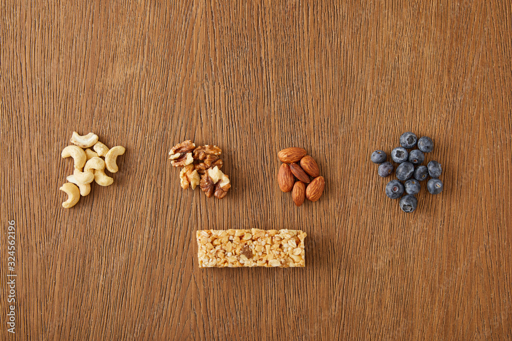 Top view of walnuts, almonds, cashews, blueberries and cereal bar on wooden background Top view of walnuts, almonds, cashews, blueberries and cereal bar on wooden background