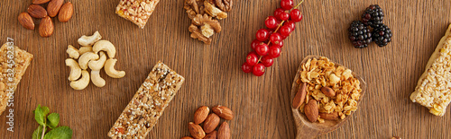 Top view of food composition of berries, nuts and cereal bars on wooden background, panoramic shot
