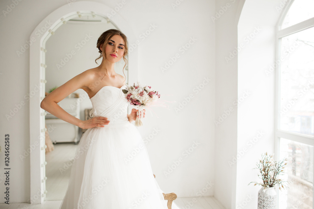 Young bride in a beautiful dress holding a bouquet of flowers in bright white studio. Wedding concept. Young bride in a beautiful dress holding a bouquet of flowers in bright white studio. Wedding concept.