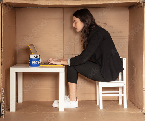 young beautiful businesswoman sitting in office cardboard box, focused working on computer