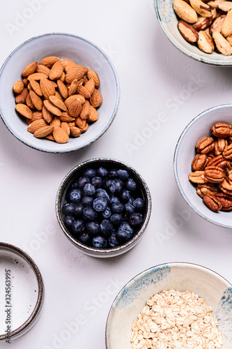 Ingredients for homemade granola: oatmeal, pecans, almond, brazilan nuts, blueberries in a bowls on grey background. Healthy diet breakfast. Flatlay. Top view. Selective focus photo