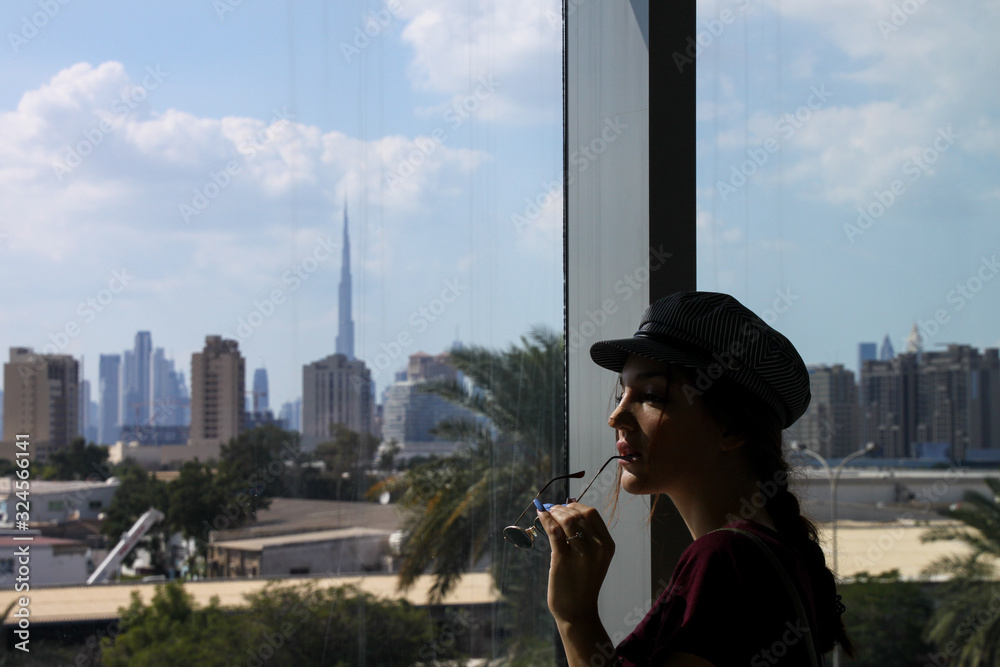 Fototapeta premium Traveling woman with hat thinking what to visit in Dubai. Dubai is in the background
