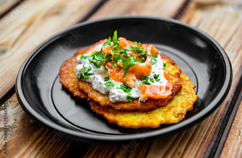 potato pancakes withsalmon fish and sour cream in a plate on wooden table